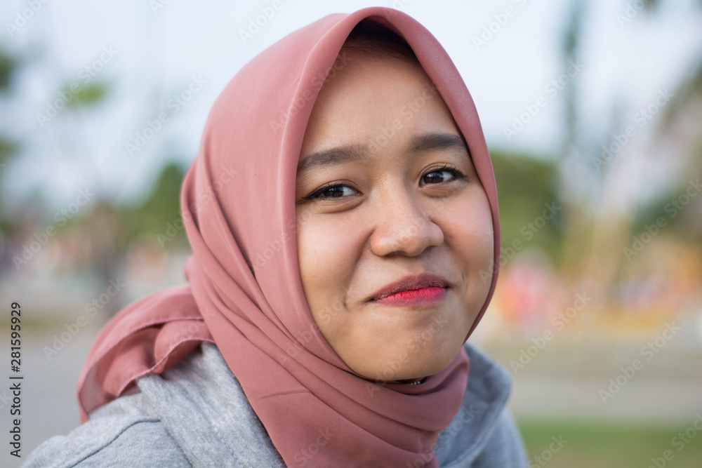 portrait of Muslim young women wearing hijabs who happily pose in front of cameras in city parks. Women see a camera with trees in the background. portrait of Muslim young women wearing hijabs who happily pose in front of cameras in city parks. Women see a camera with trees in the background.