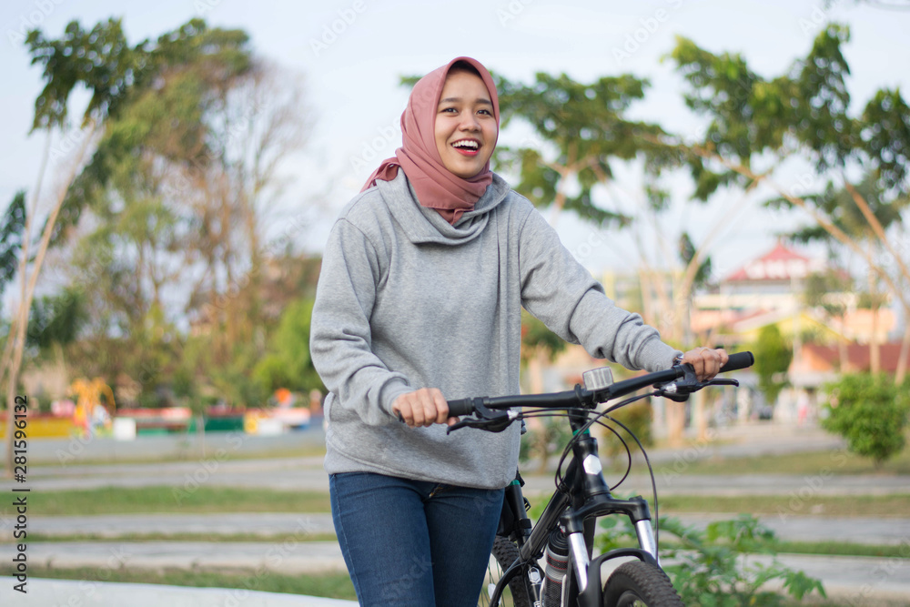 close up shot of hijab woman posing next to a bicycle and pushing her bicycle