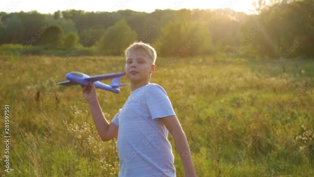 Young happy kid playing blue plastic toy plane outside on summer sunset ...