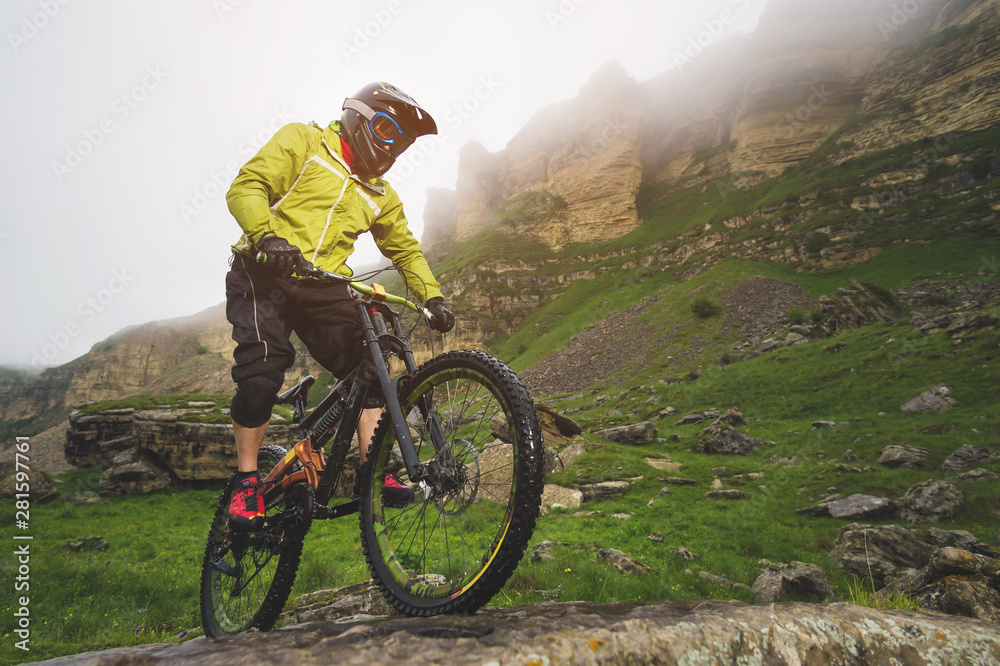 Fototapeta premium Side view wide angle partly a man on a mountain bike travels on rocky terrain Against the background of cloudy sky and epic rocks. The concept of a mountain bike and mtb downhill