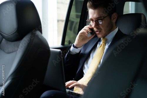 Young businessman sitting on back seat of the car, while his chauffeur is driving automobile. photo