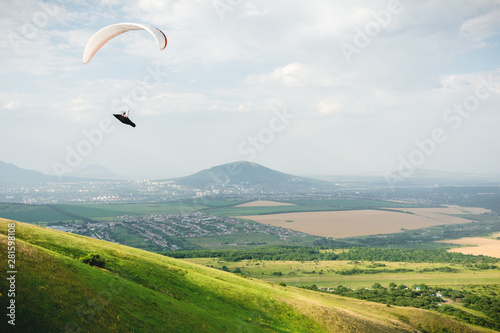 A paraglider flies in the sky in a cocoon suit on a paraglider over the Caucasian countryside with hills and mountains. Paragliding Sport Concept