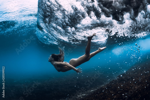 Woman swim underwater with ocean wave.