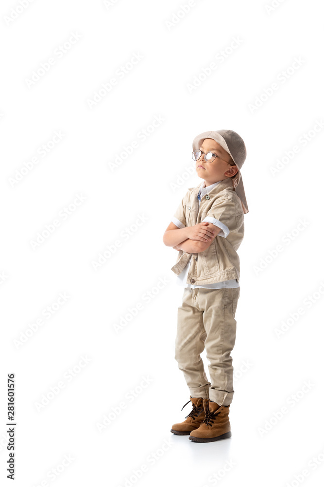 full length view of pensive explorer boy in hat and glasses with crossed arms isolated on white