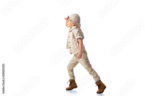 full length view of explorer boy in hat and glasses looking in distance on white