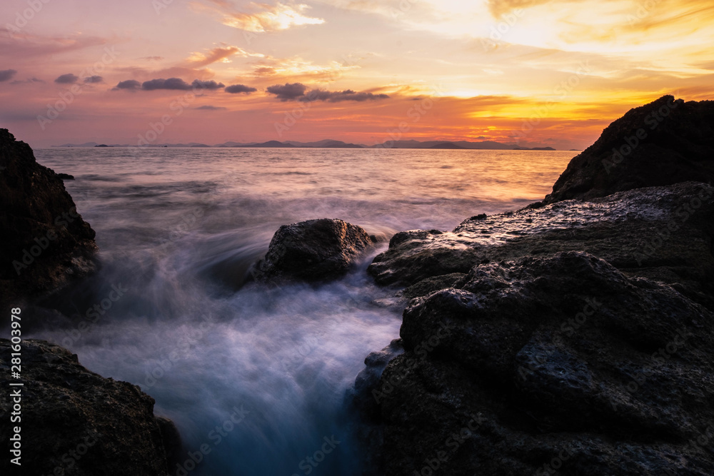 long exposure of motion ocean wave crashing on the rocks in sunset background