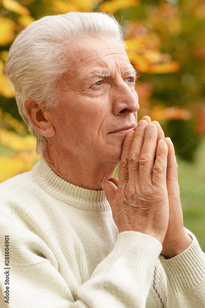 Thoughtful senior man praying in autumn park Thoughtful senior man praying in autumn park