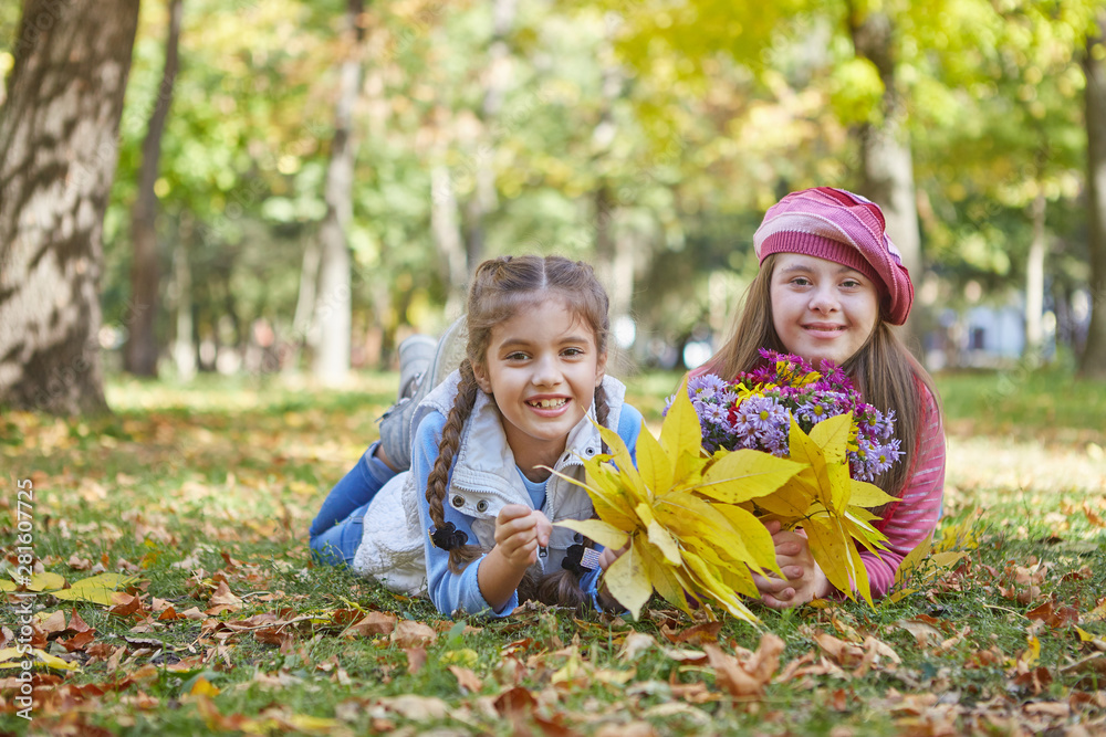 Girl with Down syndrome and little girl in autumn park.
