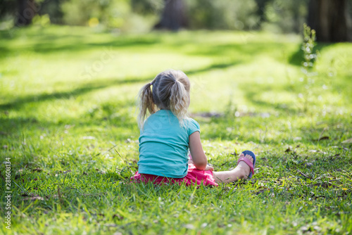 little girl sitting on grass in the park with her back turned