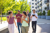 Group of young people using digital devices while walking outside. Young men and women talking on cellphones and using smartphones and tablet. Mobile technology concept