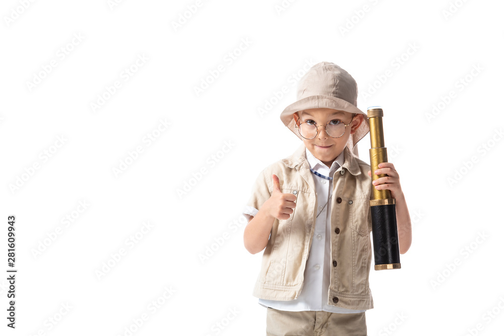 front view of smiling explorer boy in glasses and hat holding spyglass and showing thumb up isolated on white front view of smiling explorer boy in glasses and hat holding spyglass and showing thumb up isolated on white