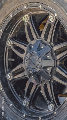 Vertical Close up view of the black rubber wheel of a vehicle parked on a sunlit road