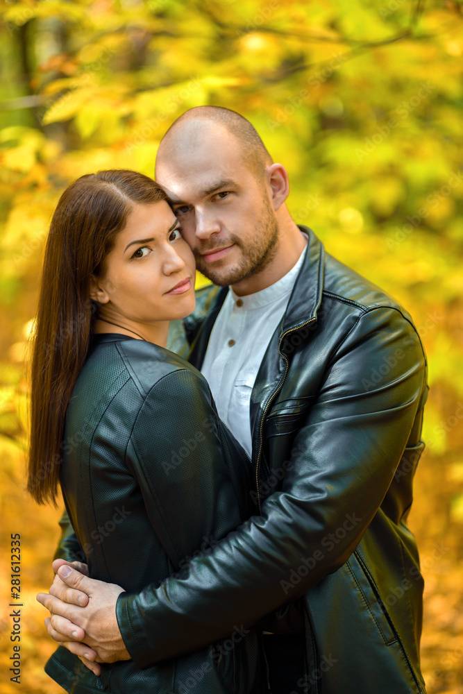 Portrait. Autumn forest. Yellow autumn background.A pair of dark-haired girl and a bald brutal man hugging in the autumn forest. A man and a woman hugging. Vertical photography Portrait. Autumn forest. Yellow autumn background.A pair of dark-haired girl and a bald brutal man hugging in the autumn forest. A man and a woman hugging. Vertical photography
