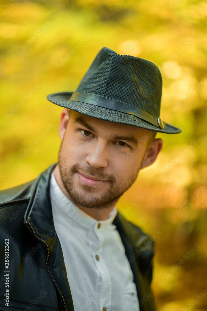 Portrait of a smiling man in a black hat and leather jacket on a yellow autumn background looking at the camera. Autumn background. Smiling young man. Vertical photo
