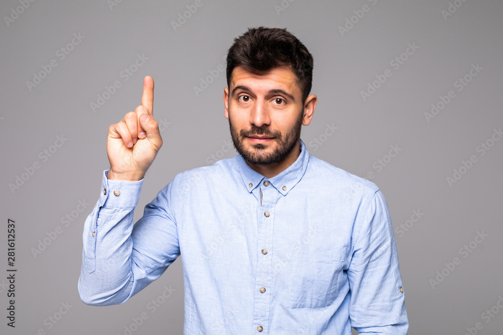 Attractive young man in blue t-shirt pointing up with his finger isolated on gray background Attractive young man in blue t-shirt pointing up with his finger isolated on gray background