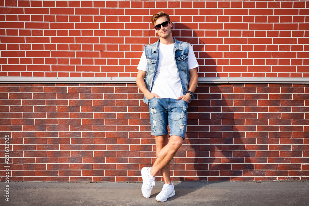 casual young man stands with his back against a brick wall. casual young man stands with his back against a brick wall.