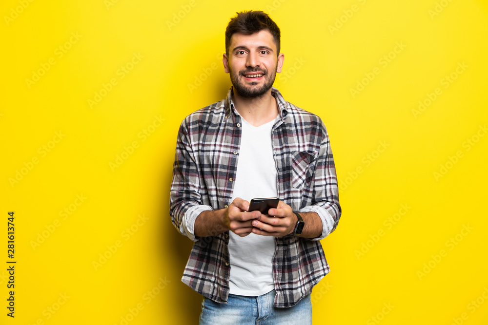 Portrait of a smiling young man holding mobile phone isolated over yellow background Portrait of a smiling young man holding mobile phone isolated over yellow background