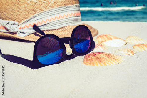 Vintage summer wicker straw beach hat and sun glasses on the sand with seashells, tropical sea background