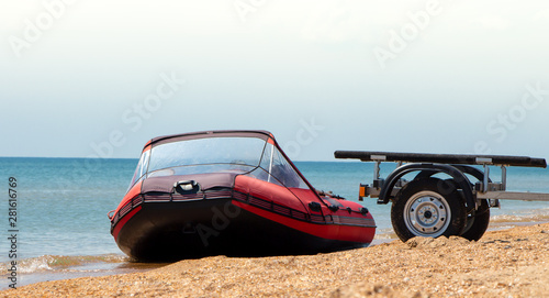 Red inflatable boat and boat trailer on the seashore.