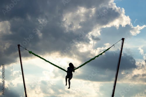Girl jumping on an extreme swing. The girl flies launched by a rubber slingshot. The girl is experiencing adrenaline and joy from the jump. Woman on a background of clouds in flight.