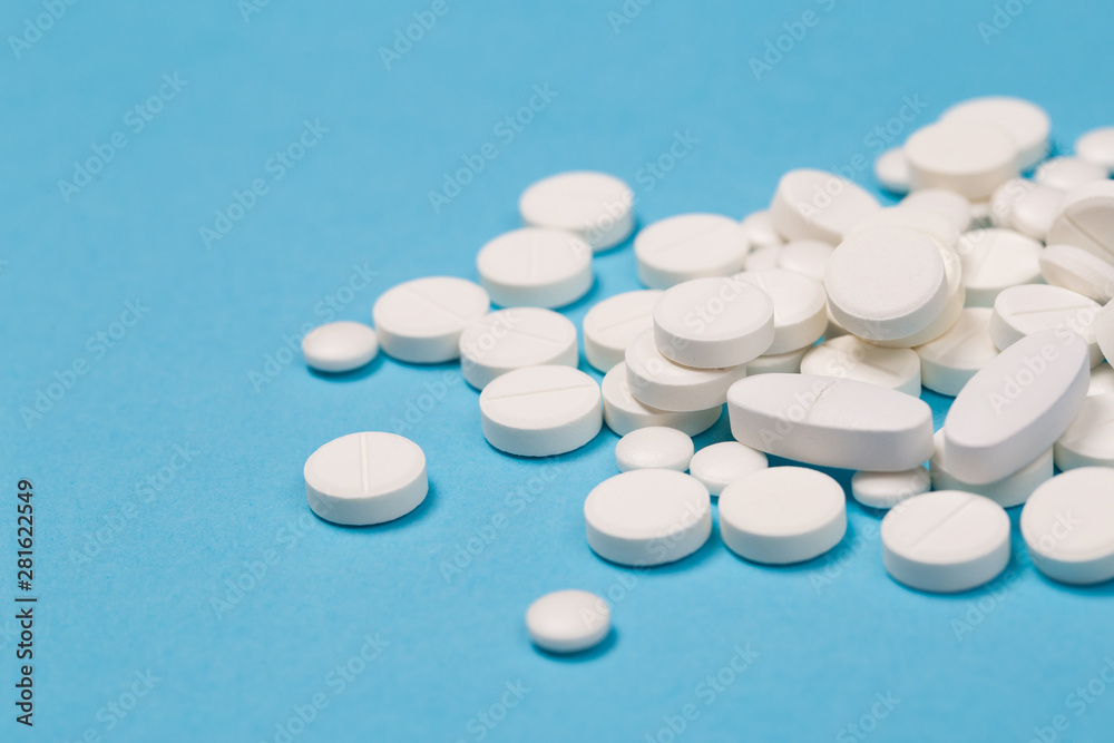 White Pills are scattered over a blue background. Close up. Medical background. - obrazy, fototapety, plakaty 