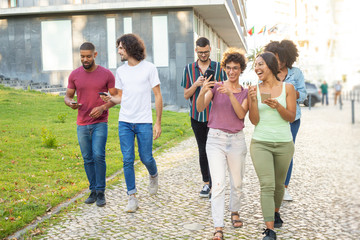 Multiethnic team walking outdoors and having fun. Men and women with mobile phones walking down street, using smartphones and taking selfie. Digital gadgets using concept