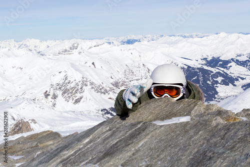 Snowboarder in orange ski goggles in a white helmet climbs to the top and extends a helping hand in the Alps mountains. On the background of mountains.