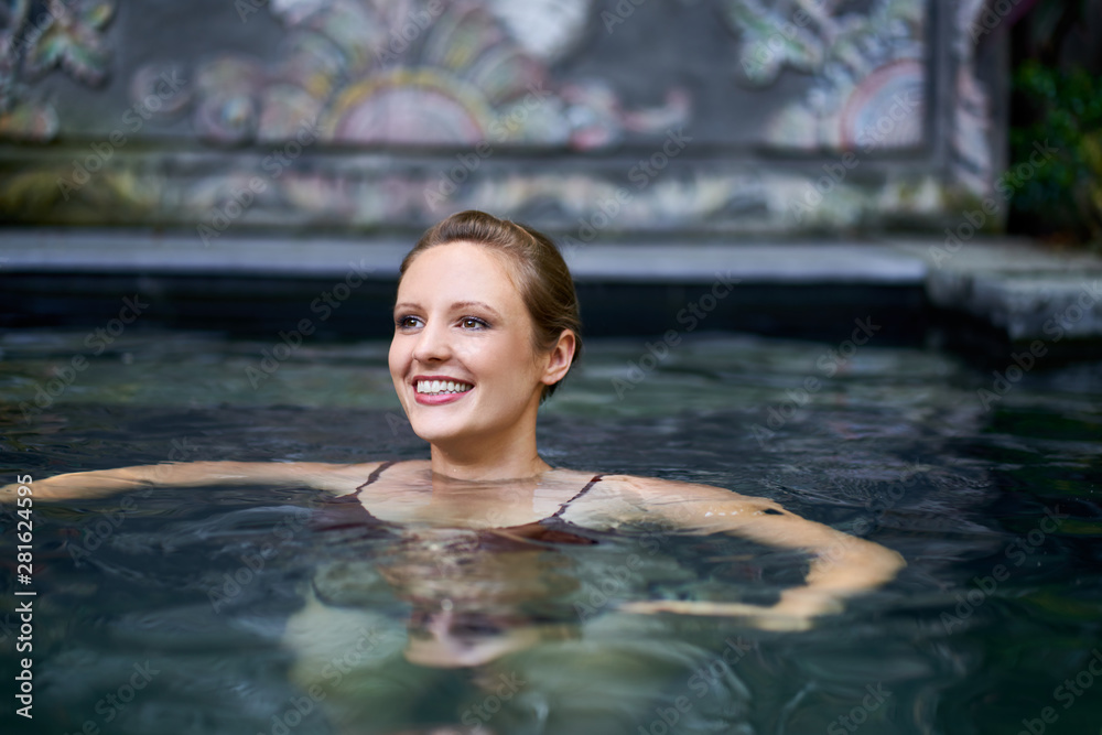 Young smiling woman swimming outdoors in exotic spa pool of luxurious hotel during tropical vacation in Bali