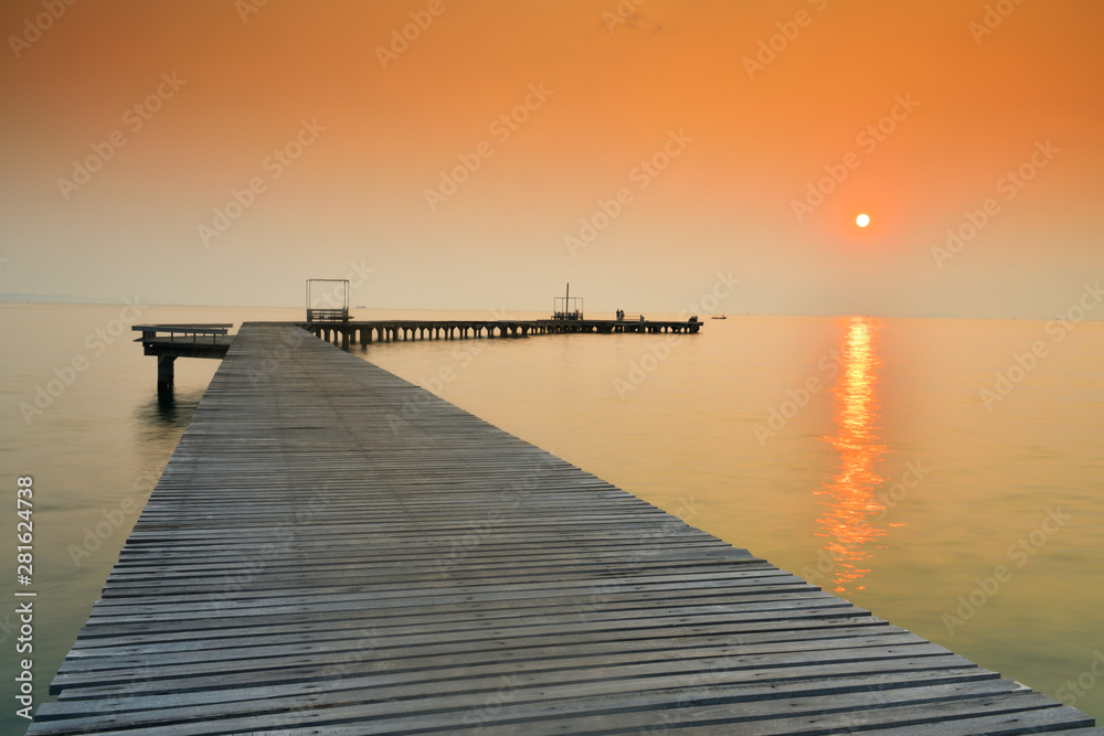 Fototapeta premium Wooden bridge that stretches into the sea at sunrise.