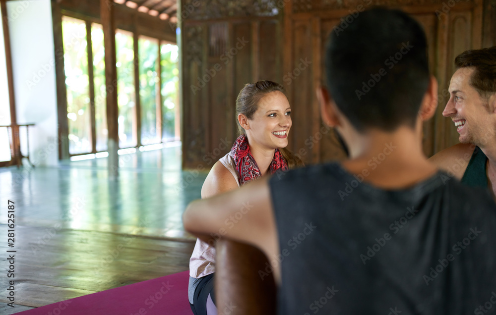 Candid shot of beautiful female meditation teacher discussing with mixed-race male students about yoga course and Indonesian culture in Bali