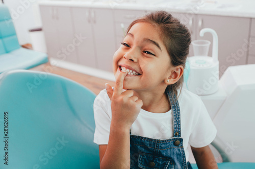 Mixed race little patient showing her perfect toothy smile while sitting dentists chair photo