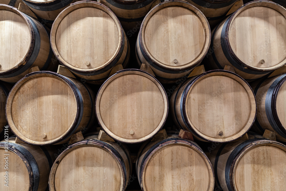 Wooden wine oak barrels stacked in straight rows in order, old cellar of winery, vault. Concept brewery background, professional degustation, winelover, sommelier travel, copyspace, place for text