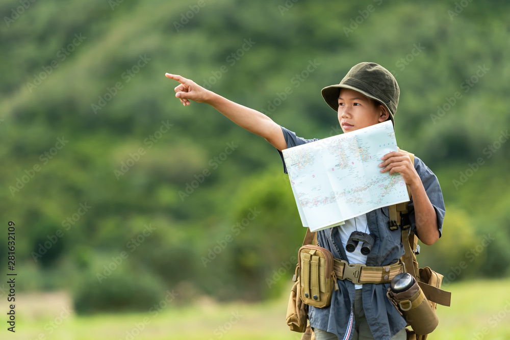 Asian boy backpack checking map and pointing in jungle forest, trips adventure and tourism for destination and leisure for education and relax in nature park .  Travel vacations Concept - obrazy, fototapety, plakaty 