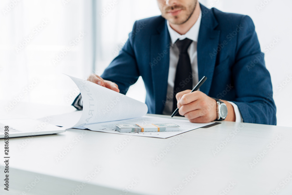 cropped view of man holding pen and contract near bribe on table cropped view of man holding pen and contract near bribe on table