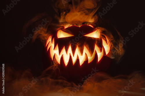 Fuming bright Jack-o'-lantern pumpkin on dark solid background. Glowing eyes and a terrible grin. Halloween minimal concept. Copy space. Desktop wallpapers