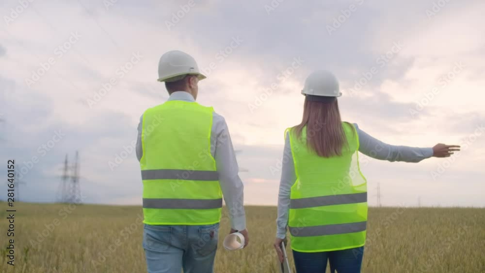 The view from the back: group of engineers at a high-voltage power plant with a tablet and drawings walk and discuss a plan for the supply of electricity to the city.