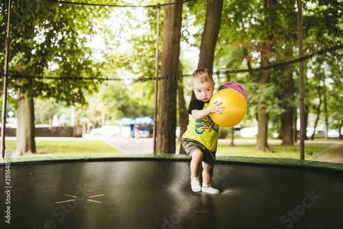 happy and smiling two-year-old boy jumps on a trampoline in the park in summer while walking with his family