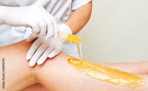 Cosmetologist beautician waxing female legs in the spa center beauty salon