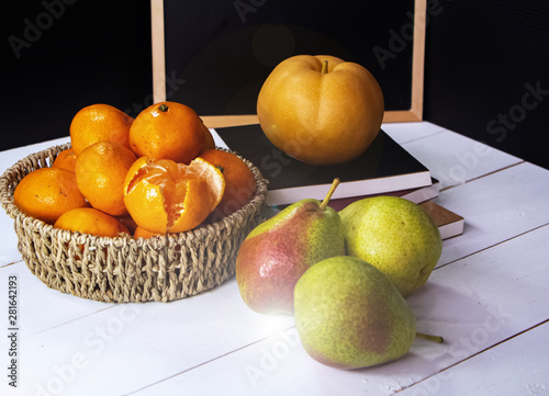 Group of orange fruit put in woven basket,beside blurred Chinese pear,on white timber board,blurry light around photo