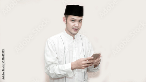 portrait of handsome asian muslim man with head cap and using smartphone taking a call and smile at camera