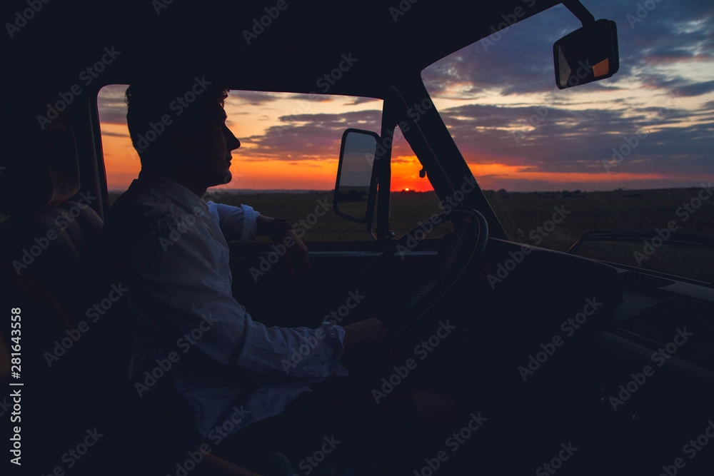 Silhouette of man driving a car on sunset background. Travel and Adventure
