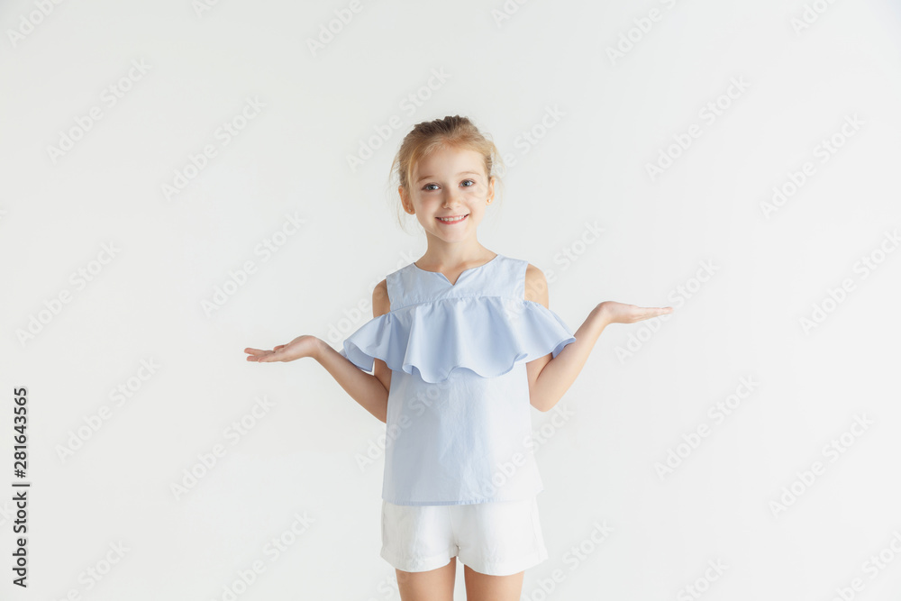 Stylish little smiling girl posing in casual clothes isolated on white studio background. Caucasian blonde female model. Human emotions, facial expression, childhood. Showing empty space, inviting