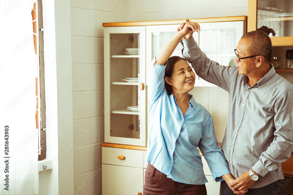 Asian senior couple is dancing and smiling while cooking together in kitchen. Asian senior couple is dancing and smiling while cooking together in kitchen.