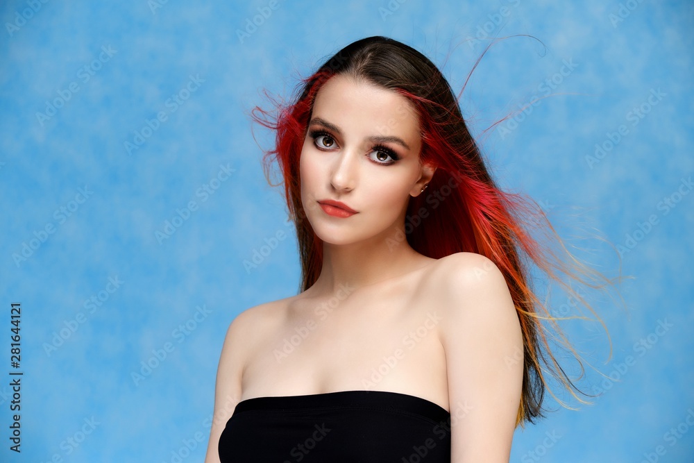 Studio portrait of a model with perfect makeup and colored hair on a blue background. Beautiful female face of a pretty girl. Perfect makeup. Skin care. Fashionable cosmetics.