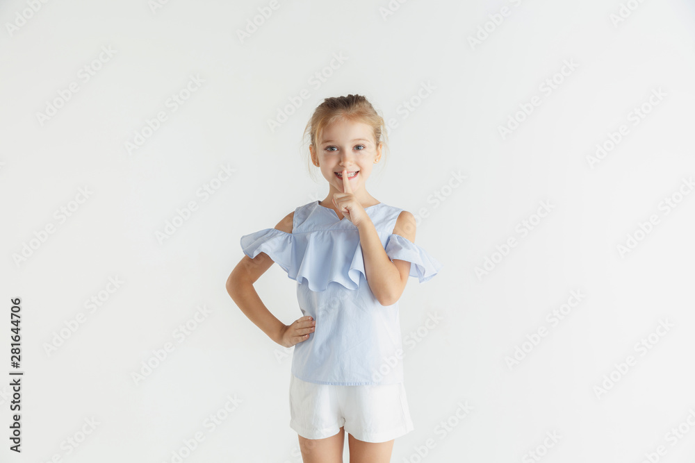 Stylish little smiling girl posing in casual clothes isolated on white studio background. Caucasian blonde female model. Human emotions, facial expression, childhood, sales concept. Whispering a Stylish little smiling girl posing in casual clothes isolated on white studio background. Caucasian blonde female model. Human emotions, facial expression, childhood, sales concept. Whispering a