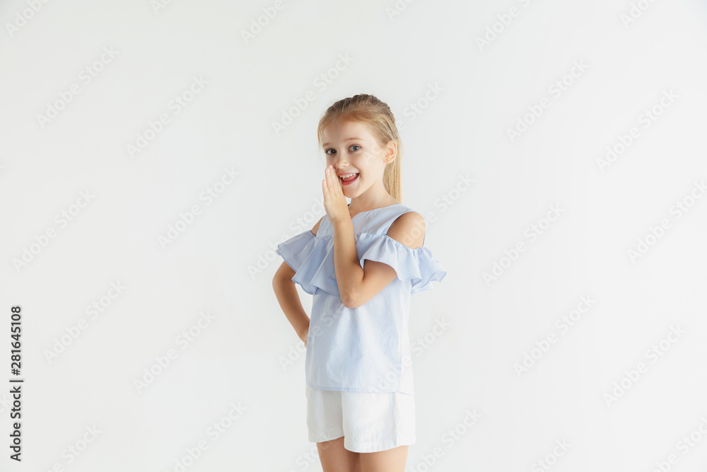 Stylish little smiling girl posing in casual clothes isolated on white studio background. Caucasian blonde female model. Human emotions, facial expression, childhood, sales concept. Whispering a Stylish little smiling girl posing in casual clothes isolated on white studio background. Caucasian blonde female model. Human emotions, facial expression, childhood, sales concept. Whispering a