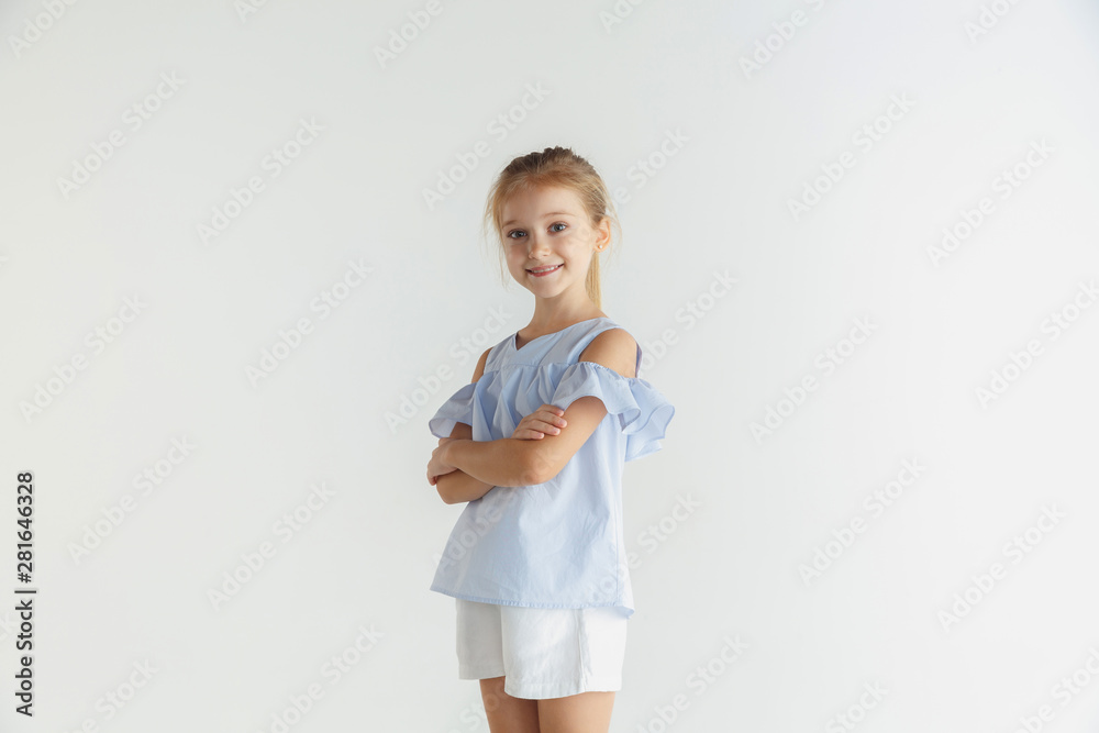 Stylish little smiling girl posing in casual clothes isolated on white studio background. Caucasian blonde female model. Human emotions, facial expression, childhood, sales. Standing with hands