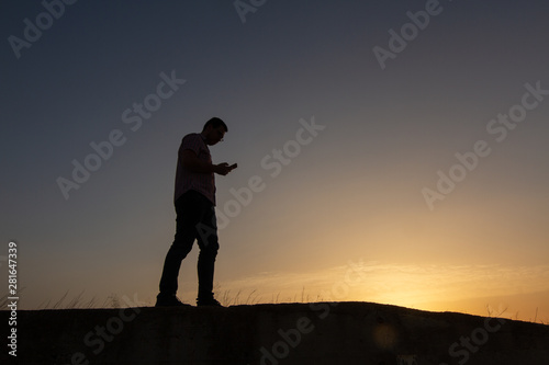 silhouette of man with cell phone at sunset