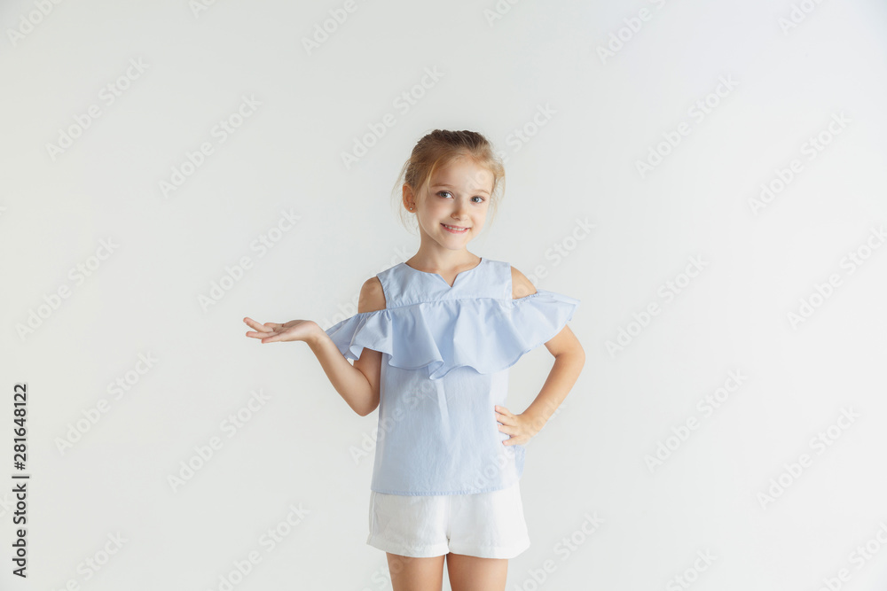 Stylish little smiling girl posing in casual clothes isolated on white studio background. Caucasian blonde female model. Human emotions, facial expression, childhood. Showing empty space, inviting