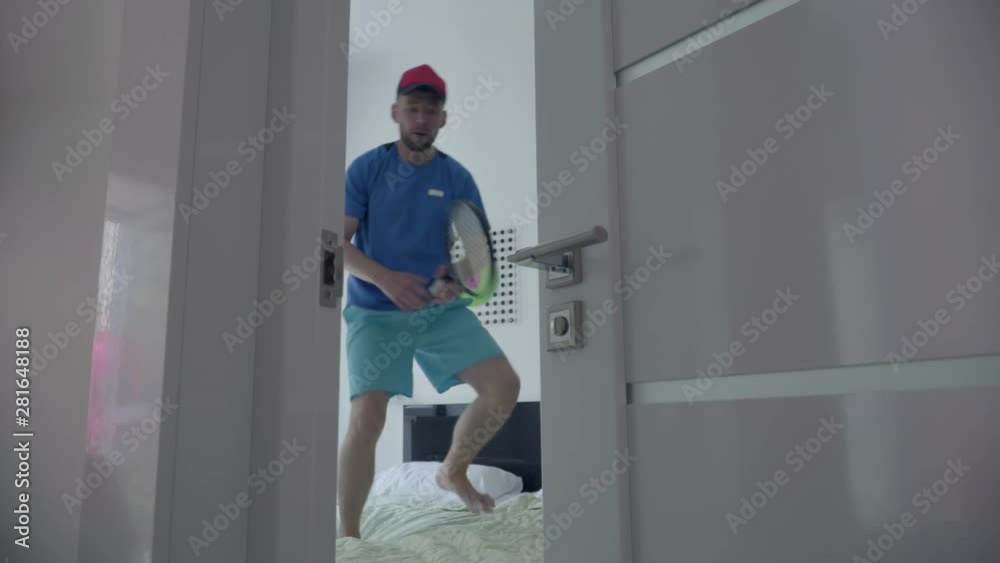 Young man training to play tennis standing on the bed in comfortable hotel room. Active lifestyle. Sports and recreation.